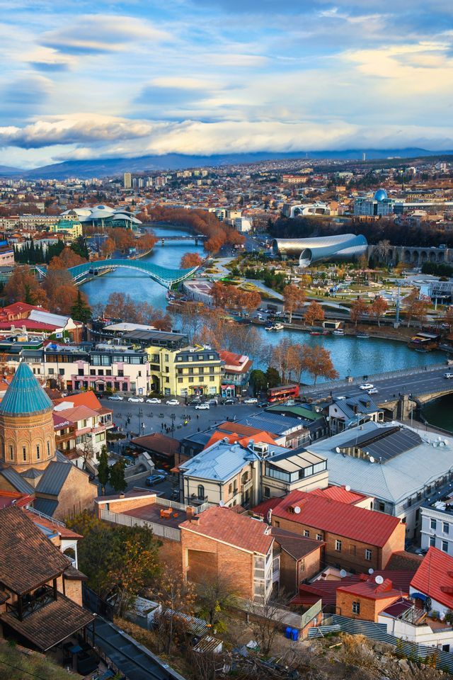 Una vista aerea di una città attraversata da un fiume, che mostra un'architettura diversificata, dalle chiese antiche agli edifici moderni.