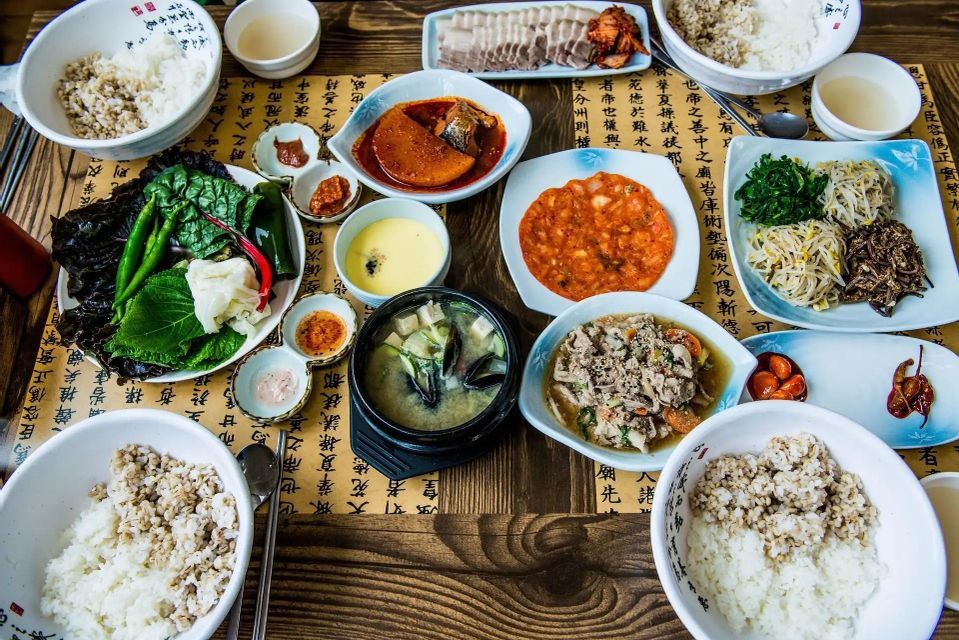 An overhead view of a traditional Korean meal, including rice, soup, sliced pork, and various side dishes on a wooden table.