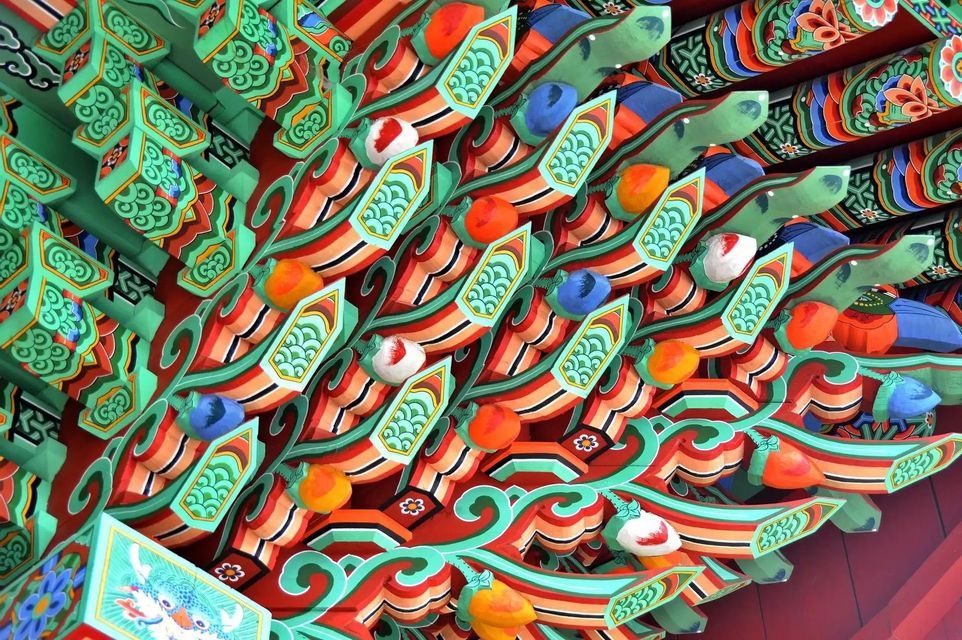 A close-up of the colorful, intricately painted wooden eaves of a traditional Asian building, featuring green, red, and blue patterns.