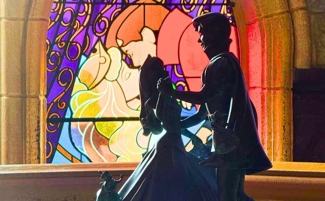 Eine Silhouettenstatue eines tanzenden Paares vor einem großen, farbenprächtigen Buntglasfenster in einem Steingebäude.