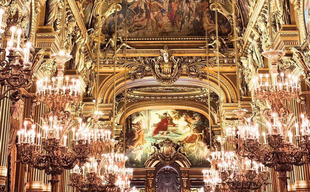 L'interno dorato e sfarzoso di un teatro dell'opera, con lampadari illuminati, intagli intricati e dipinti classici.