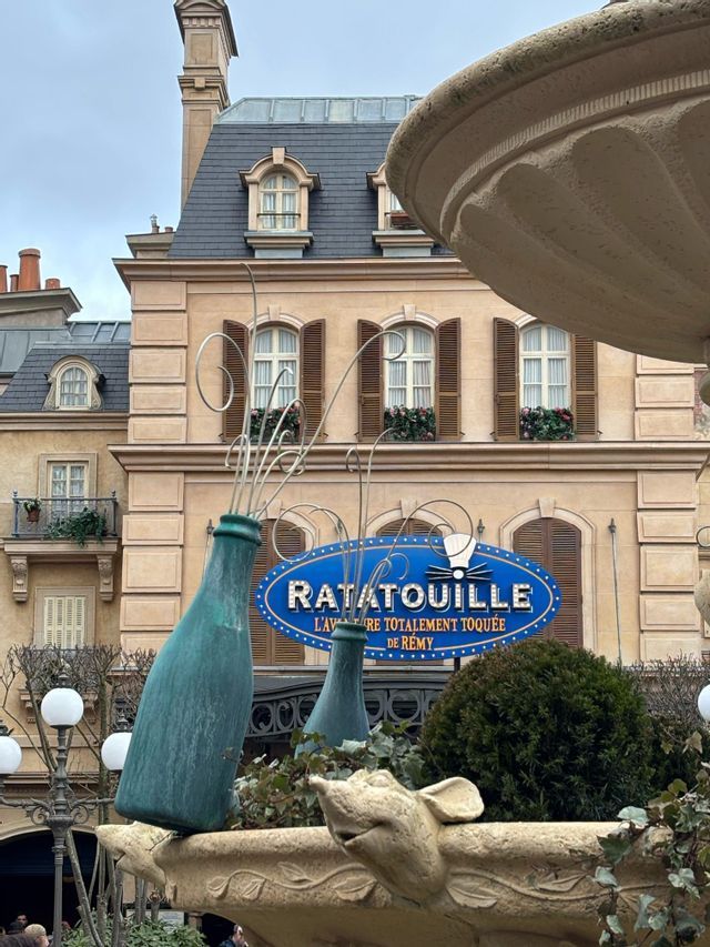 Der Eingang zur Ratatouille-Attraktion, mit einem großen blauen Schild vor einem Gebäude im Pariser Stil und einem thematischen Brunnen.