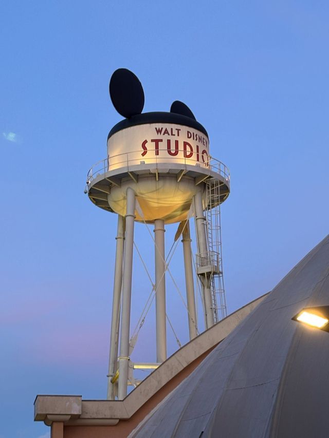 Der Wasserturm der Walt Disney Studios mit großen Micky-Maus-Ohren, beleuchtet vor einem dämmrigen Himmel.
