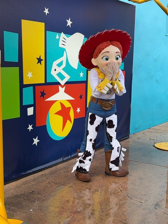 Jessie di Toy Story in costume posa con le mani alla bocca davanti a una parete grafica colorata.