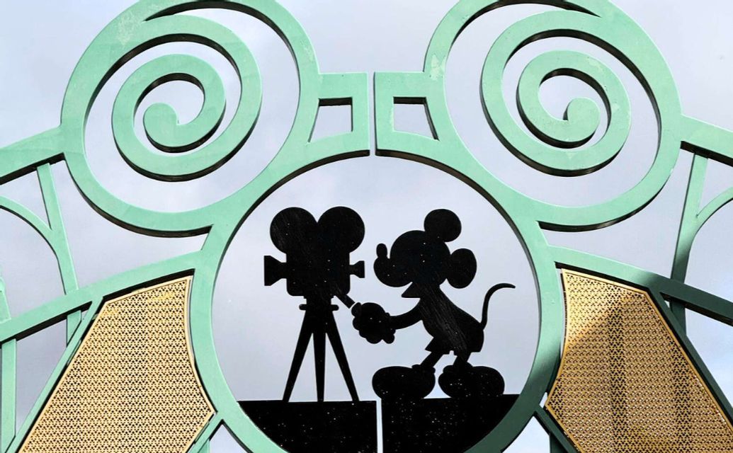 Nahaufnahme eines grünen Metalltors mit einer schwarzen Silhouette von Micky Maus, die eine Vintage-Filmkamera bedient.