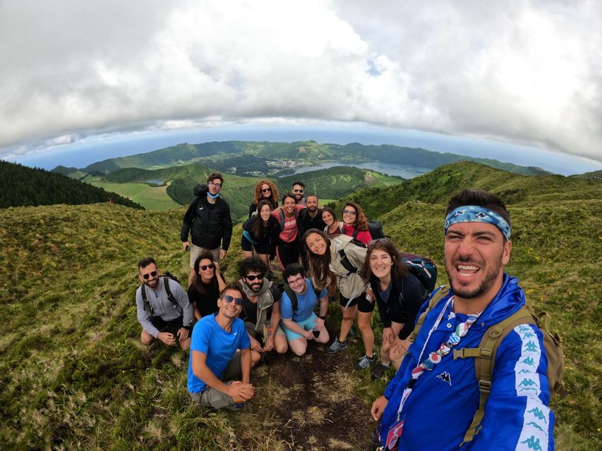 Un grupo de WeRoad se toma una selfie panorámica en una colina, con un lago de cráter y la costa de fondo.