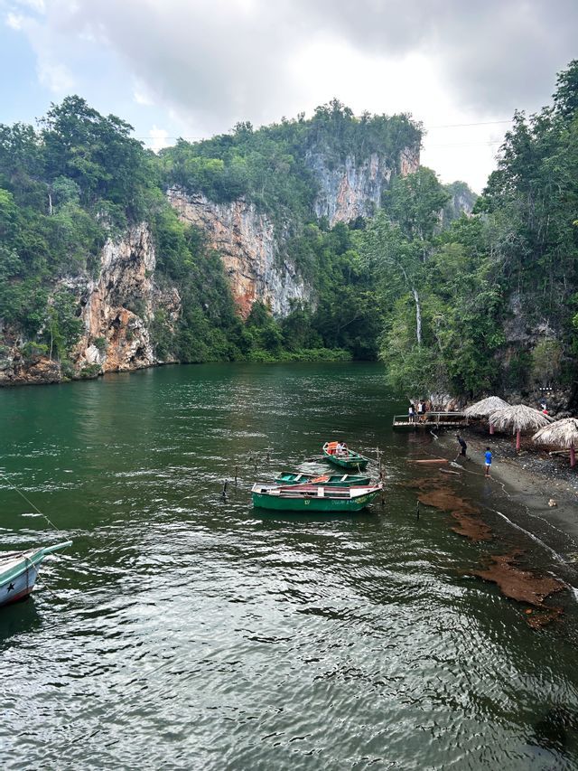 Un viaggio di gruppo WeRoad si riunisce su un piccolo molo vicino a un fiume, con barche verdi ormeggiate nell'acqua e una lussureggiante parete rocciosa alle spalle.