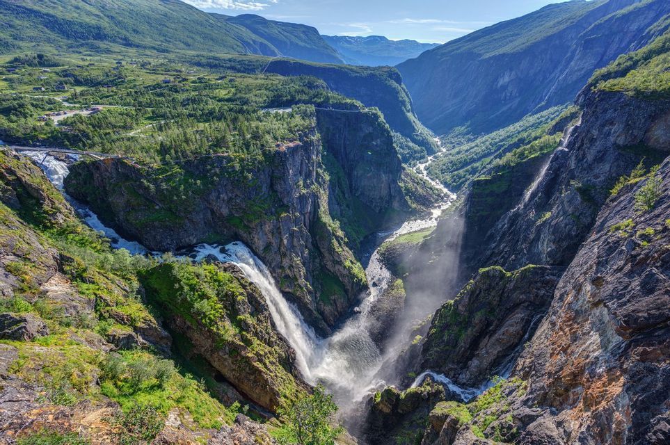 Una grande cascata si getta in un profondo canyon, con un fiume che scorre in una lussureggiante valle di montagna.
