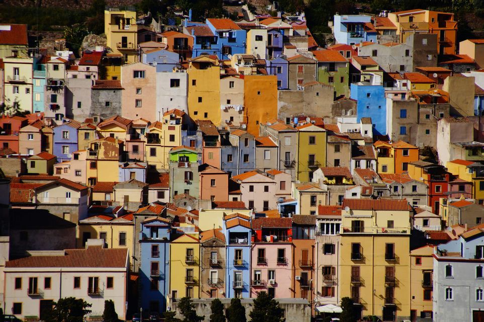 Un fitto insieme di case colorate con tetti rossi che ricopre una collina soleggiata.