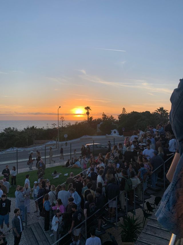 Un viaggio di gruppo WeRoad radunato su gradini e una collina erbosa, mentre ammirava il tramonto sul mare.