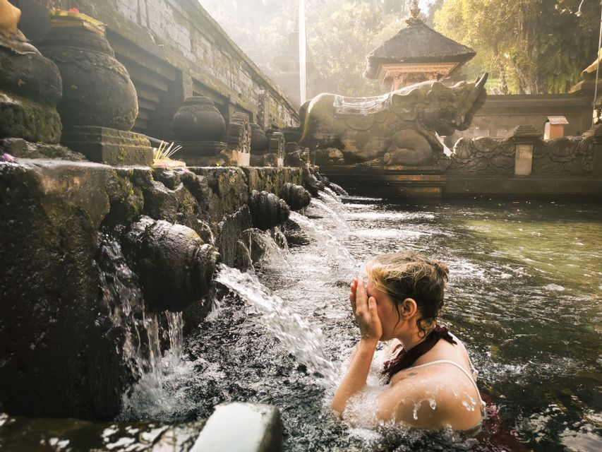 Eine Frau wäscht ihr Gesicht mit Wasser aus alten Steinspeiern in einer heiligen Quelle an einem Tempel.