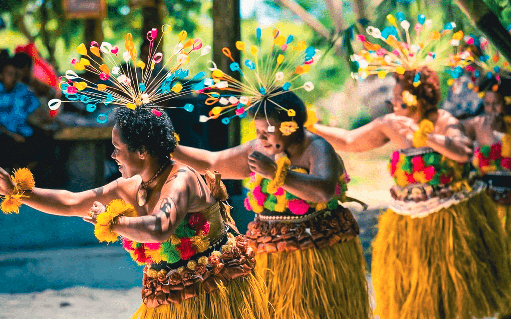 Un gruppo di danzatrici in abiti tradizionali colorati e con elaborati copricapi si esibisce in un ambiente all'aperto.