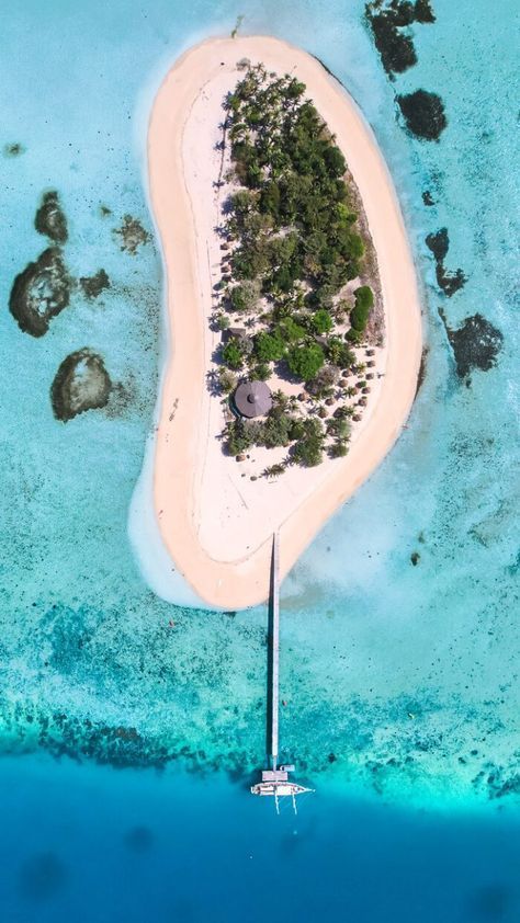 Una vista aerea dall'alto di un'isola tropicale con una spiaggia di sabbia e un lungo molo che conduce a una barca in acque limpide e turchesi.