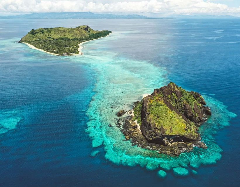 Una vista aerea di due isole lussureggianti e verdi, una grande e una piccola, circondate da barriere coralline turchesi e dall'oceano blu profondo.