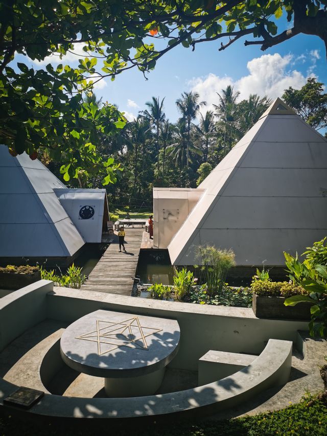 Ein sonniger Innenhof mit zwei großen weißen Pyramidenbauten, umgeben von üppiger tropischer Vegetation und einem kleinen Teich.