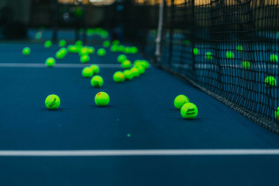 Palline da tennis verde brillante sparse su un campo blu, vicino alla rete.