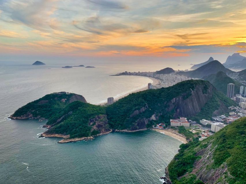 Una vista panoramica di una città costiera con una spiaggia a mezzaluna, circondata da montagne verdi e dal mare al tramonto.