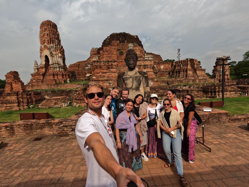 A man takes a selfie with a WeRoad group trip in front of a large Buddha statue and ancient temple ruins.