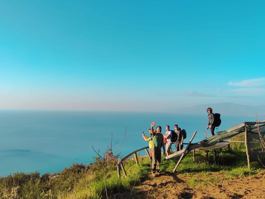 Un viaggio di gruppo WeRoad con zaini in posa su un sentiero costiero con vista sul mare blu sotto un cielo sereno.