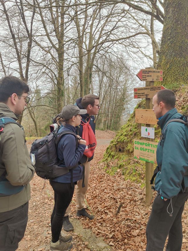 Un gruppo WeRoad di quattro persone con zaini in spalla osserva un cartello di legno su un sentiero nel bosco.