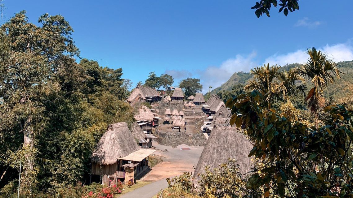 Un villaggio tradizionale con capanne coniche dal tetto di paglia costruite su terrazze di pietra, circondato da lussureggianti colline verdi sotto un cielo blu.