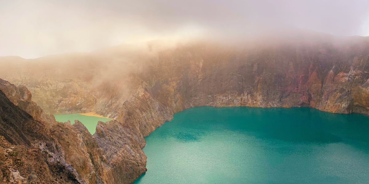 Due laghi di cratere turchesi e verdi all'interno di una grande caldera vulcanica rocciosa avvolta nella nebbia.