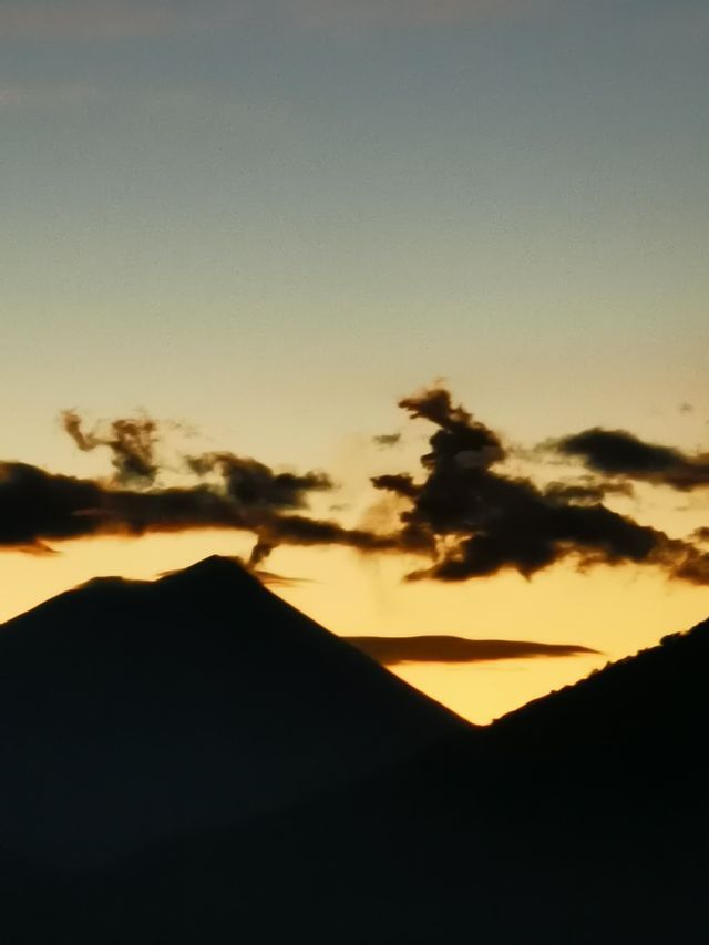 Deux sommets de montagne se profilent sur un ciel jaune et bleu au crépuscule, avec quelques nuages sombres au-dessus.