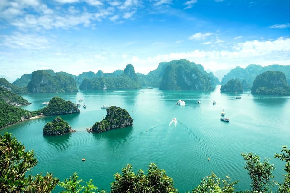 An elevated view of numerous boats sailing on turquoise water between green, rocky islands under a blue sky.