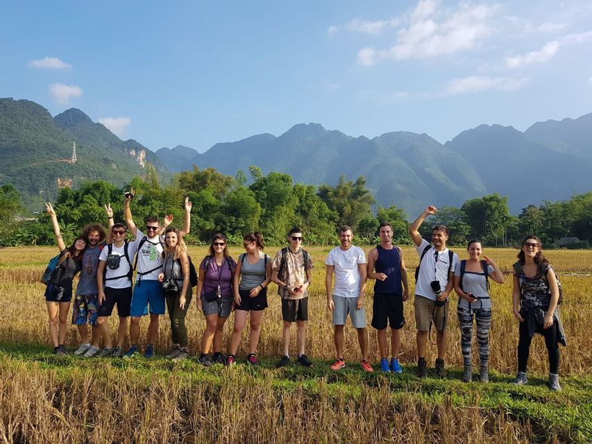 Un gruppo WeRoad in viaggio in posa per una foto in un campo dorato, con montagne verdi sullo sfondo e un cielo azzurro e limpido.