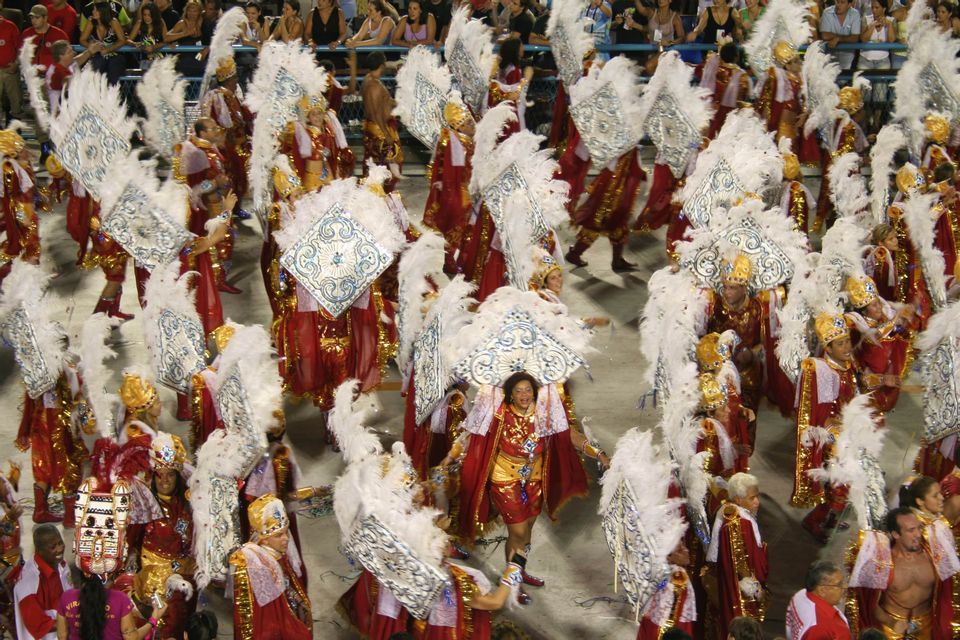 Vista dall'alto di numerosi artisti in costumi piumati rossi e bianchi durante una sfilata di carnevale.
