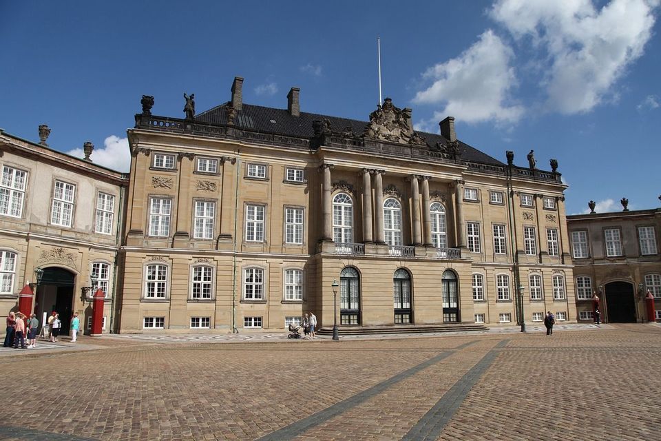 Ein großer, klassischer Palast mit einem gepflasterten Vorplatz unter einem teilweise bewölkten blauen Himmel.