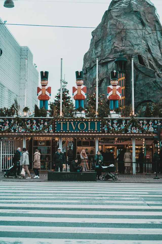 Menschen gehen und stehen auf einem Gehweg vor dem Tivoli-Eingang, der mit Lichtern und großen Nussknackerstatuen geschmückt ist.