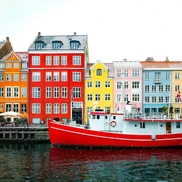 Ein rotes Boot liegt in einem Kanal vor einer Reihe farbenfroher Ufergebäude, während leichter Schnee fällt.