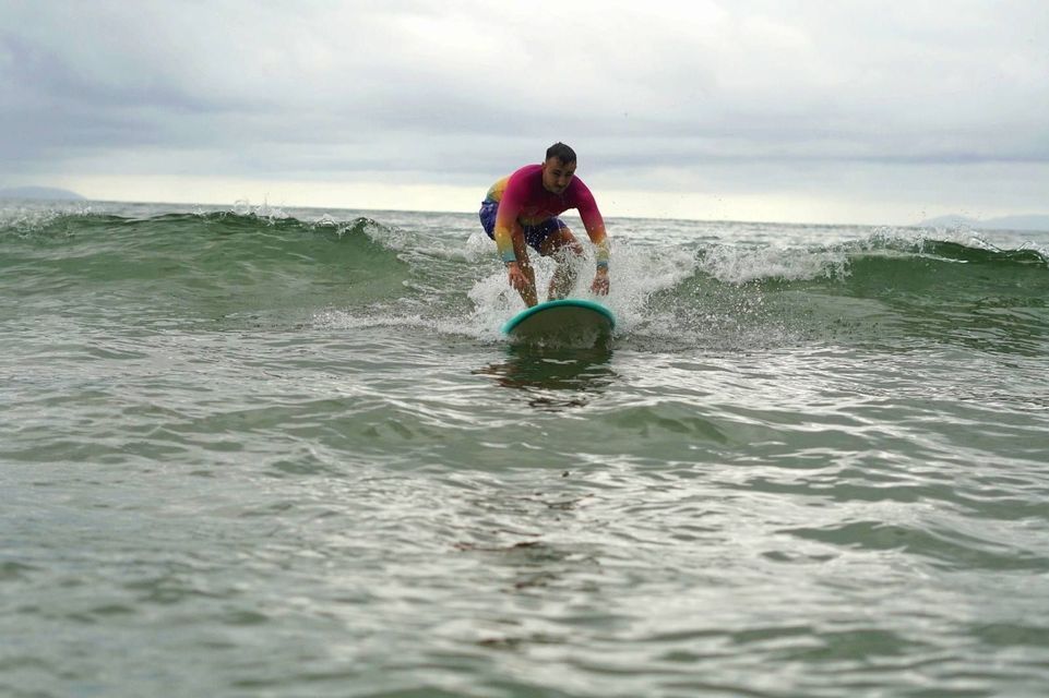 Un hombre con una camiseta de licra colorida surfea una pequeña ola en el océano bajo un cielo nublado.