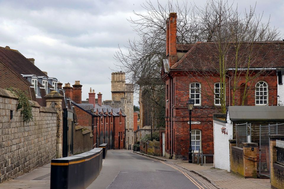 An empty street called Church Lane slopes downhill, lined with red brick buildings and a stone wall under a cloudy sky.