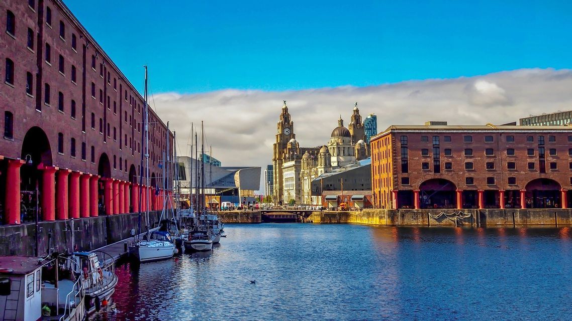 A view of a city harbor with boats moored alongside red brick buildings under a partly cloudy sky.