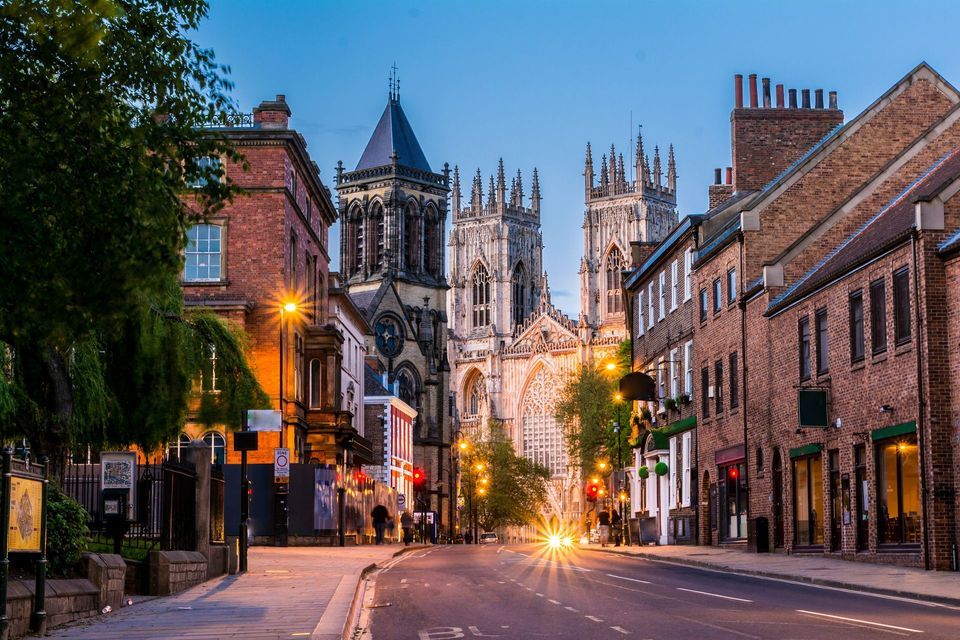 A large Gothic cathedral seen from a city street at dusk, with illuminated streetlights and car headlights.