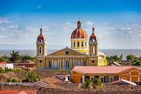 Una grande cattedrale gialla con cupole rosse si erge sopra i tetti in terracotta, con uno specchio d'acqua visibile sullo sfondo.
