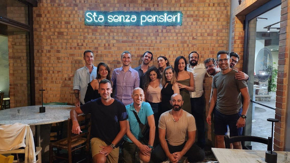 Un viaje en grupo de WeRoad posando para una foto dentro de un restaurante con una pared de ladrillo y un letrero de neón azul de fondo.