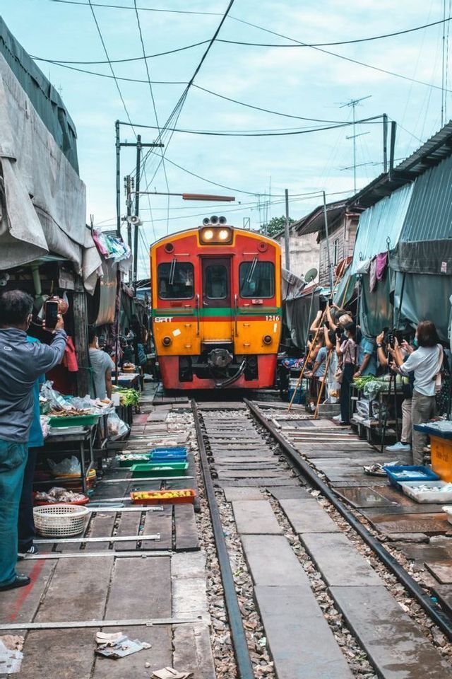 Un tren amarillo y rojo atraviesa un mercado estrecho construido a lo largo de las vías mientras la gente toma fotos.