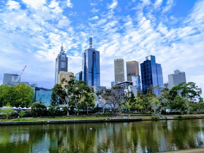 Moderne Skyline mit hohen Wolkenkratzern, vom Fluss aus gesehen, mit baumgesäumtem Park am gegenüberliegenden Ufer.