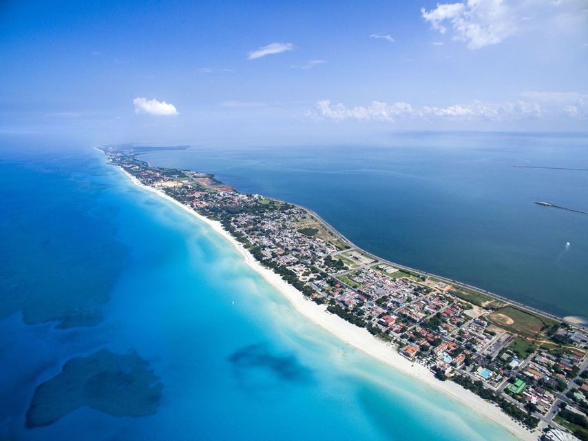 Vue aérienne d'une longue presqu'île présentant une plage de sable blanc, une ville côtière et des eaux contrastées turquoise et bleu profond.