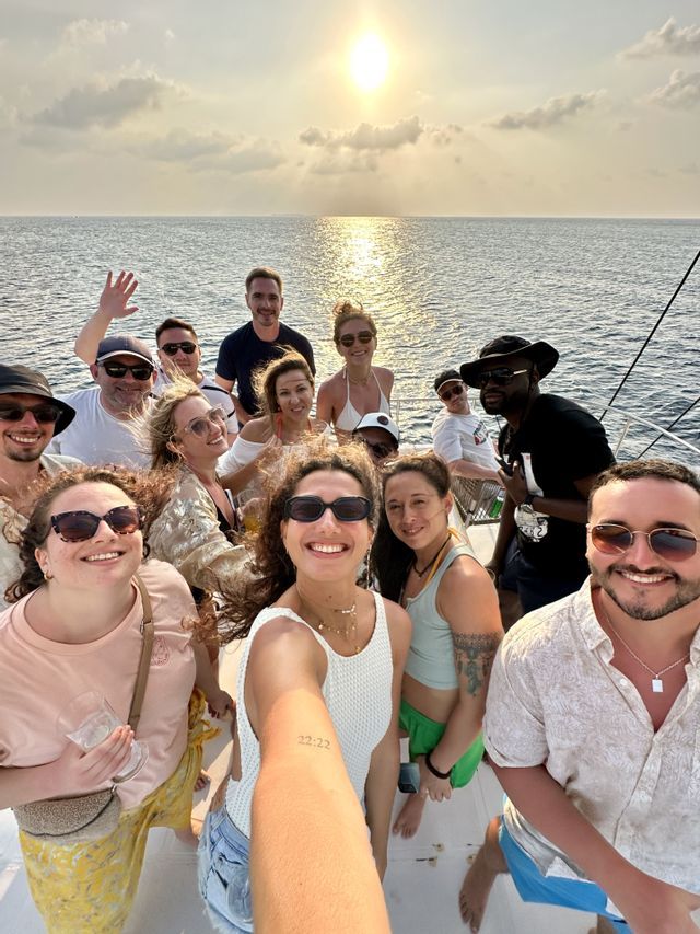 Un groupe WeRoad prend un selfie sur un bateau au coucher du soleil sur la mer.