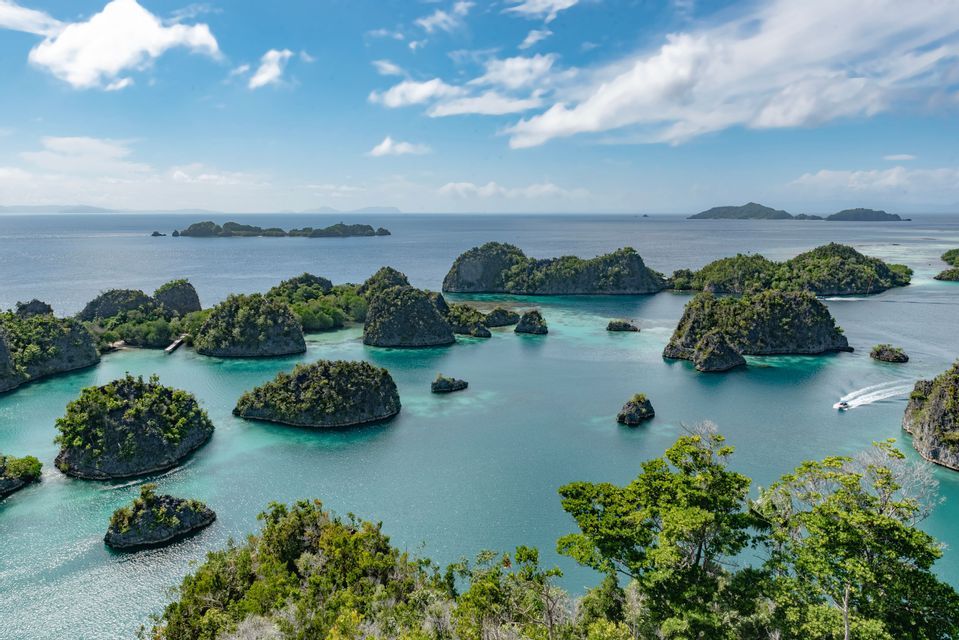 Una vista aérea de numerosas islas verdes y rocosas, dispersas en un mar turquesa bajo un cielo parcialmente nublado.