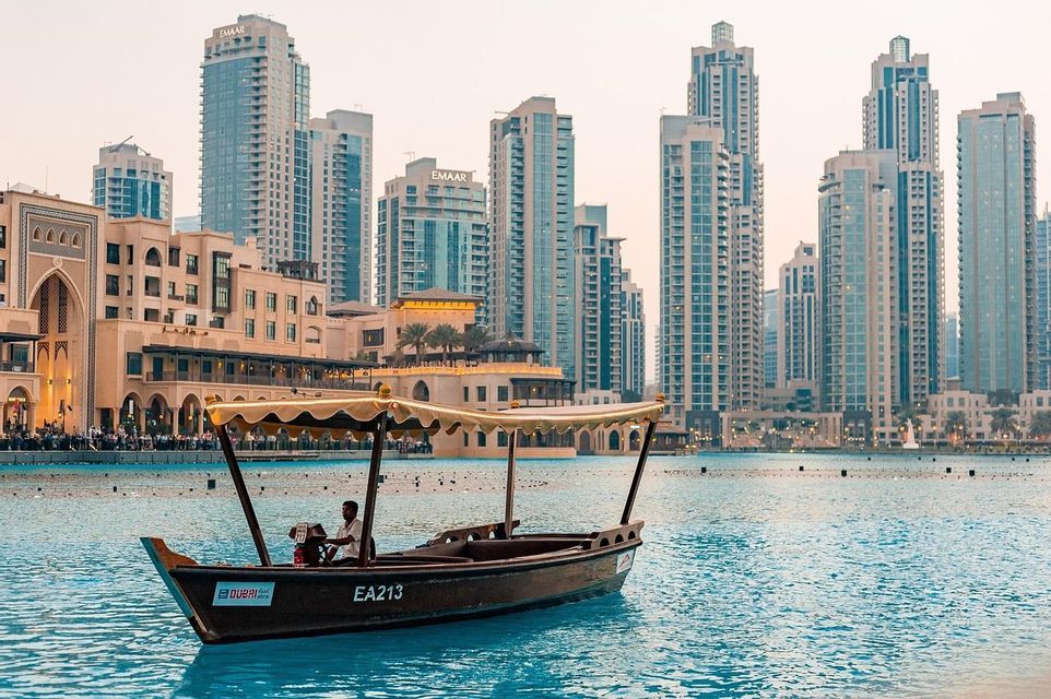 Ein traditionelles Boot mit gelbem Sonnendach schwimmt auf türkisfarbenem Wasser vor einer modernen Stadtsilhouette