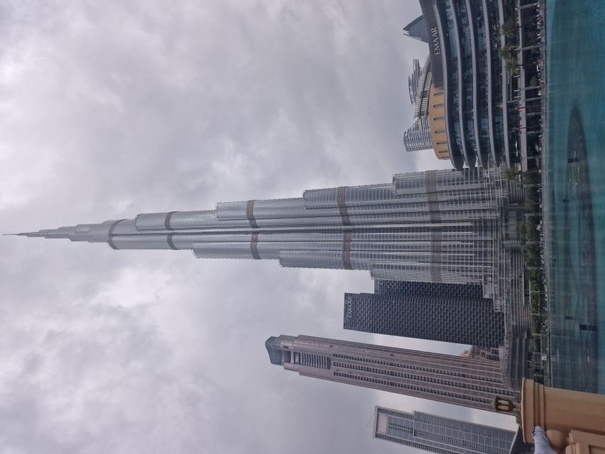 Der Wolkenkratzer Burj Khalifa ragt in einen bewölkten Himmel, umgeben von anderen modernen Gebäuden und einem Wasserbecken an seiner Basis.