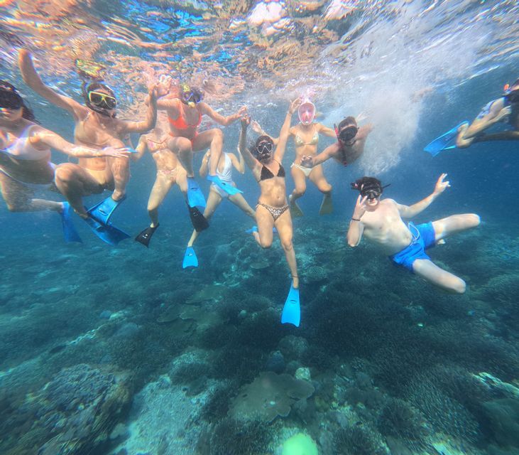 Un grupo de WeRoad de personas con equipo de snorkel posando para una foto submarina sobre un arrecife de coral.