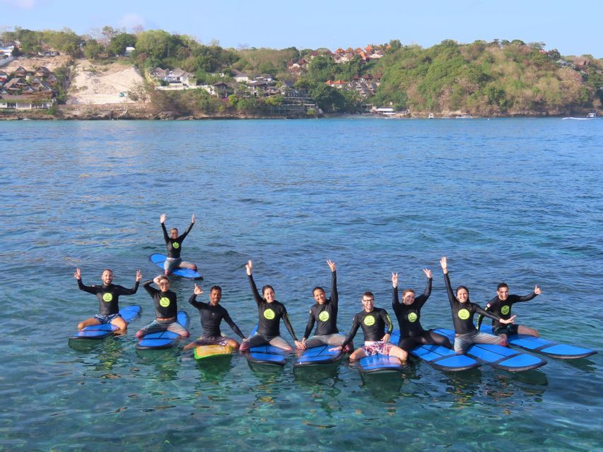 Un viaje en grupo de WeRoad con trajes de neopreno posando en tablas de surf azules en el mar claro, con una costa verde de fondo.