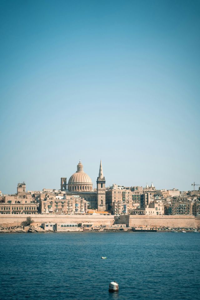 Une ville côtière avec un dôme et une flèche proéminents vus depuis l'eau bleue sous un ciel clair.