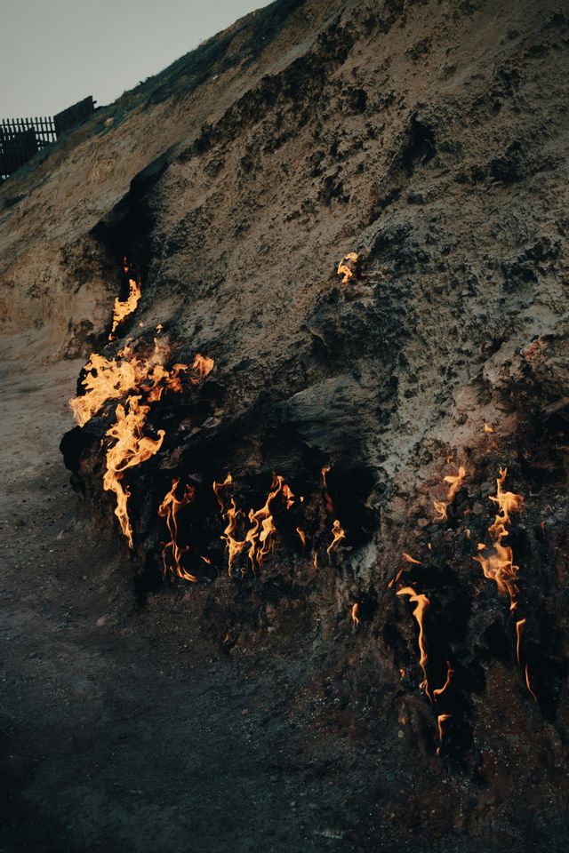 Fiamme ardono dalle crepe e fessure sul fianco di una collina rocciosa e terrosa.